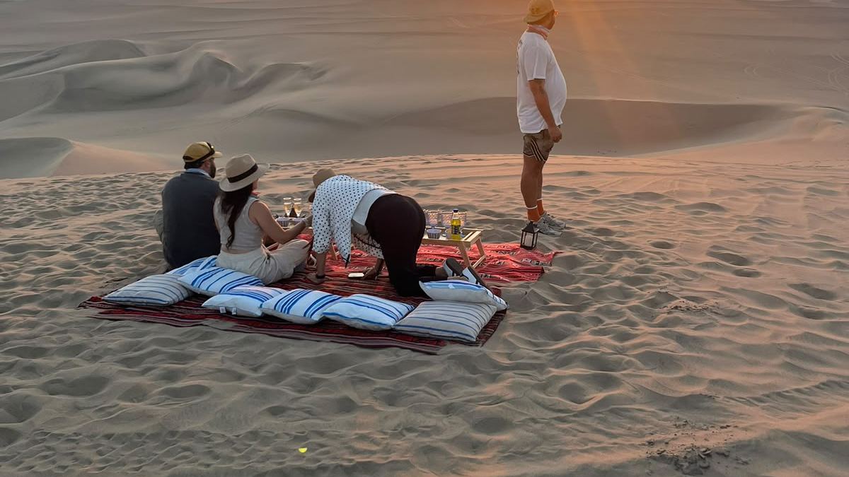 A group sitting on the sand watching the sunset over the dunes